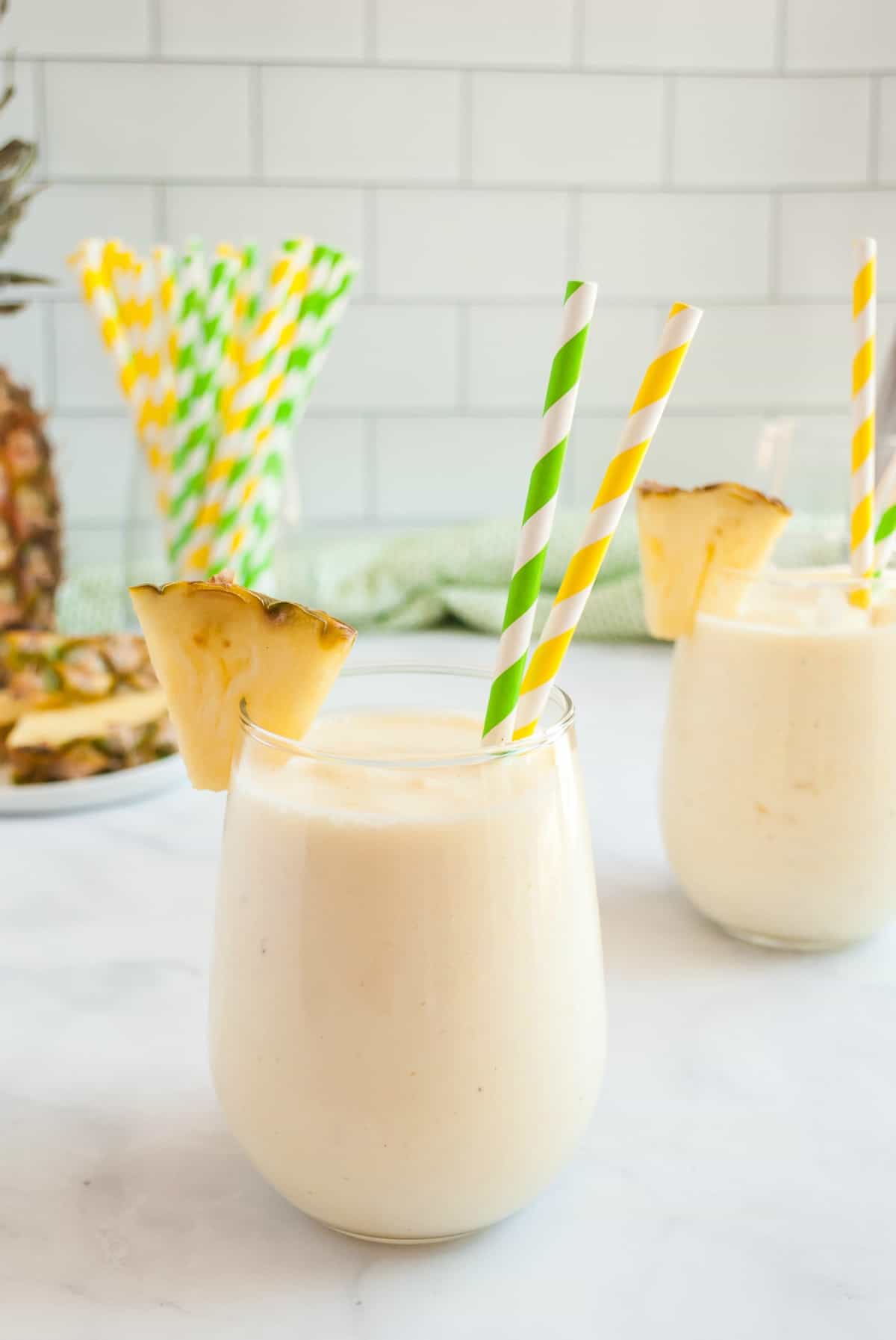 Copycat disney dole whip in a stemless wineglass garnished with a pineapple slice.