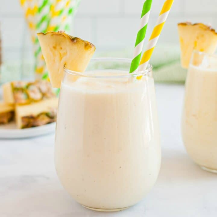 Dole whip in two stemless wineglasses garnished with fresh pineapple slices. Served with yellow and green striped paper straws.