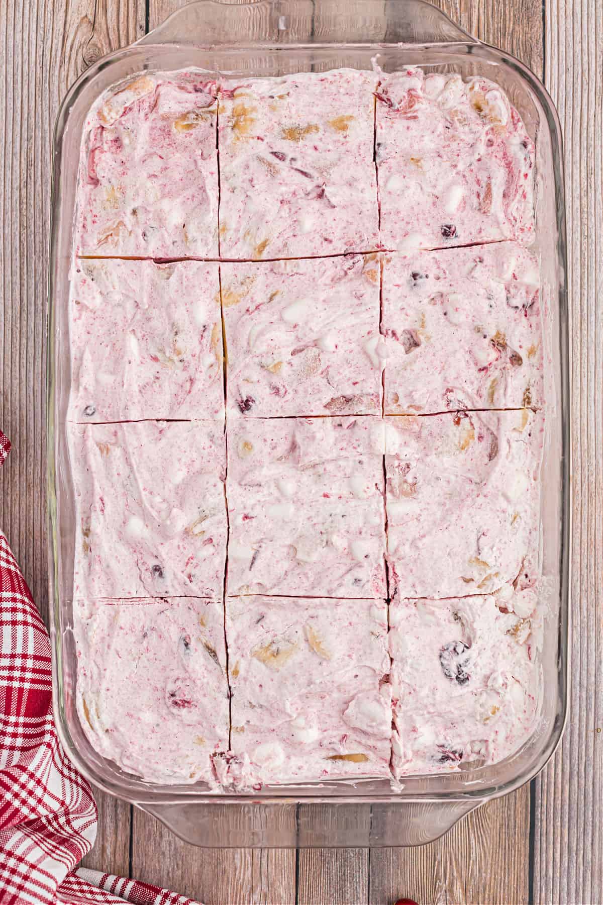 Glass 13x9 baking dish with frozen cranberry salad cut into 12 large squares.