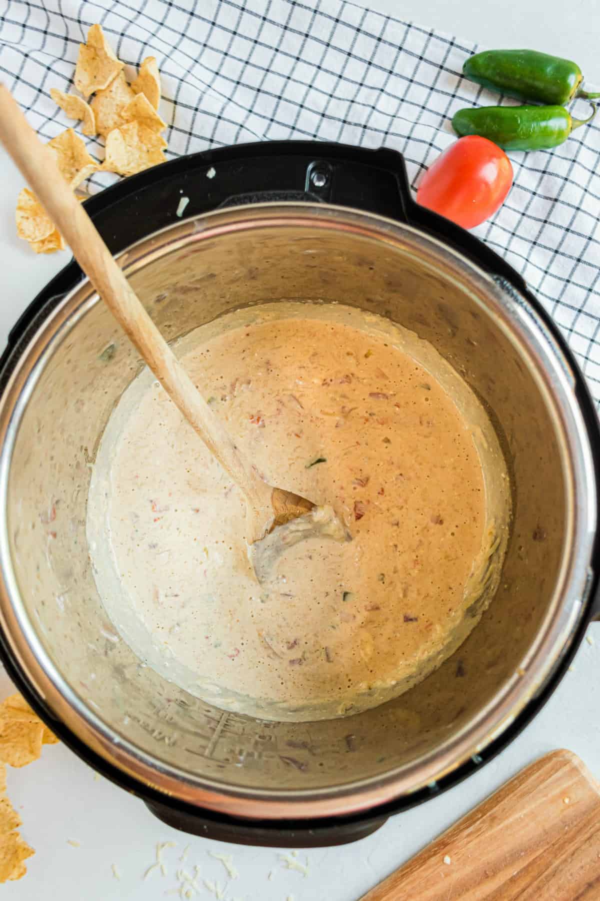 Queso smooth in the instant pot being stirred with a wooden spoon.