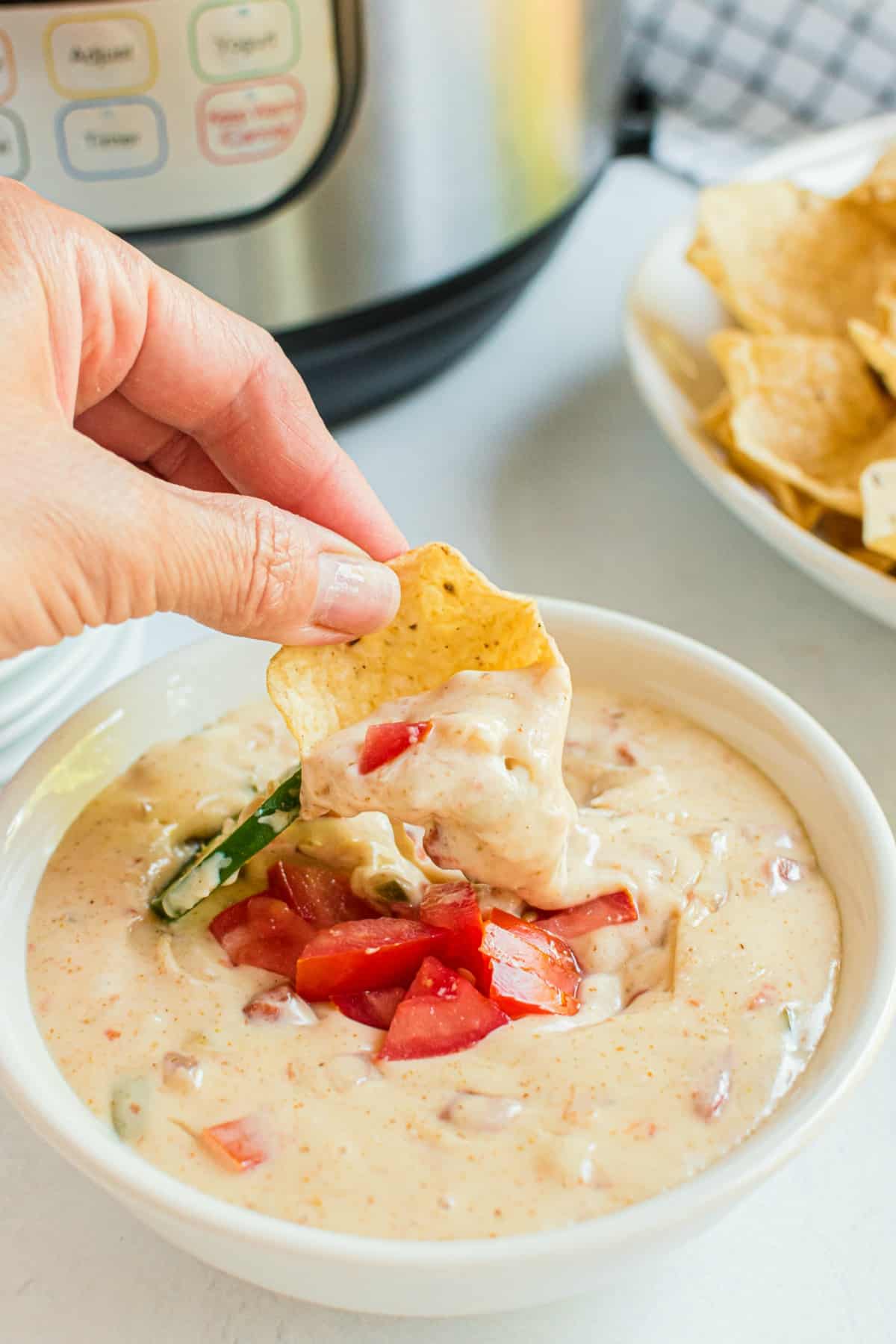 Tortilla scoop being dipped into a bowl of queso with instant pot in background.