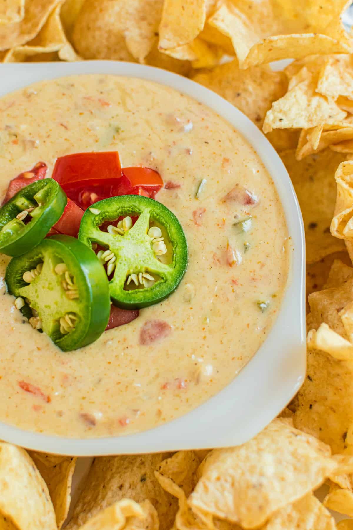 Platter of tortilla chips with a white bowl of queso in the middle. Garnish of jalapeno and rotel tomatoes on the queso.