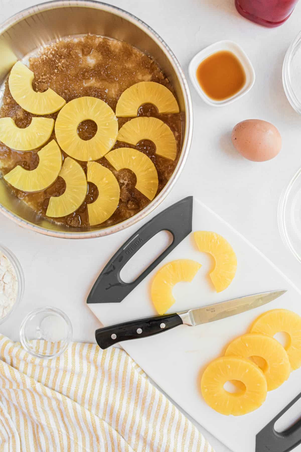 Pineapple slices being cut in half and arranged in the melted butter and brown sugar cake pan.