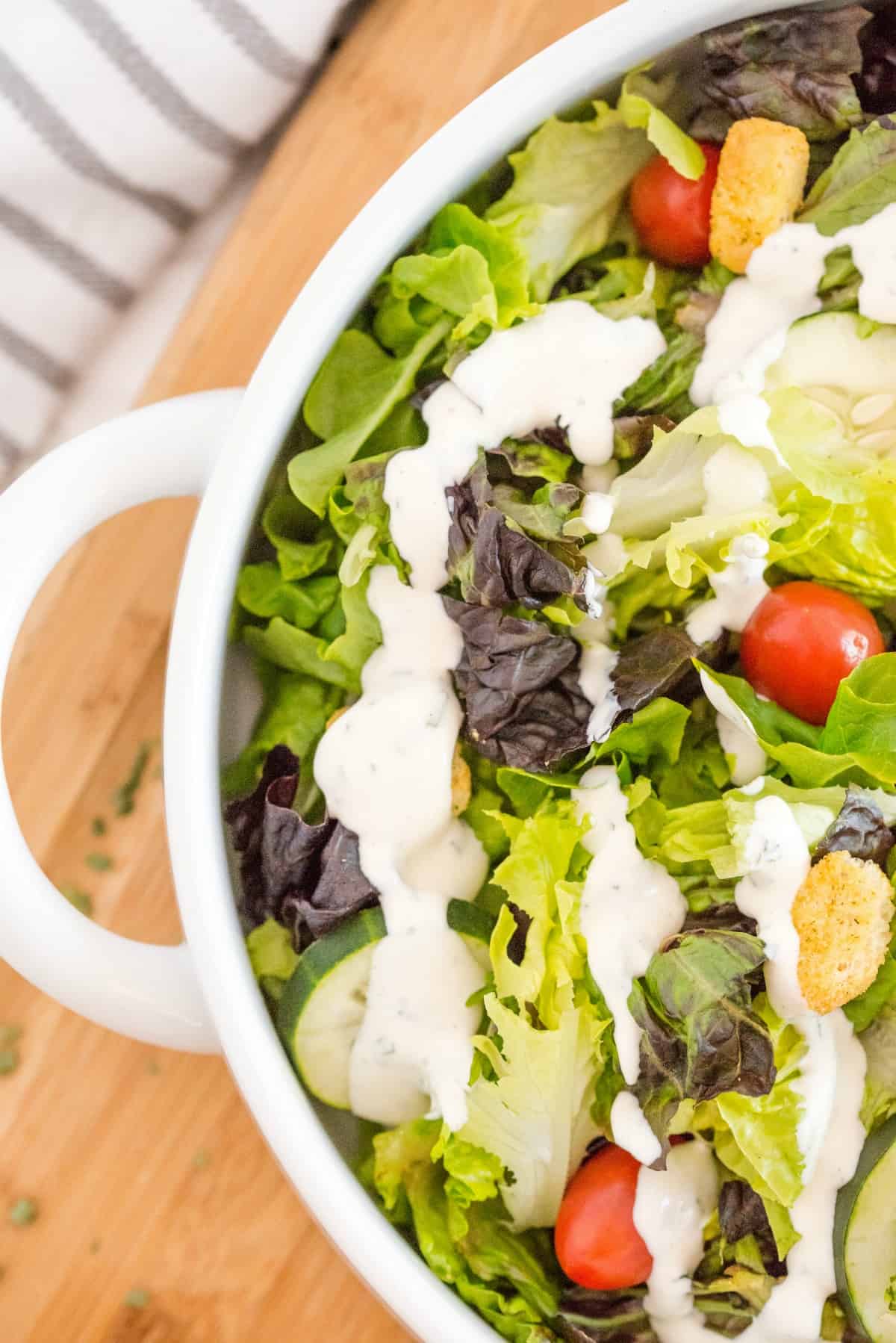 Leafy green salad in a white bowl topped with cherry tomatoes, croutons, and homemade ranch dressing.