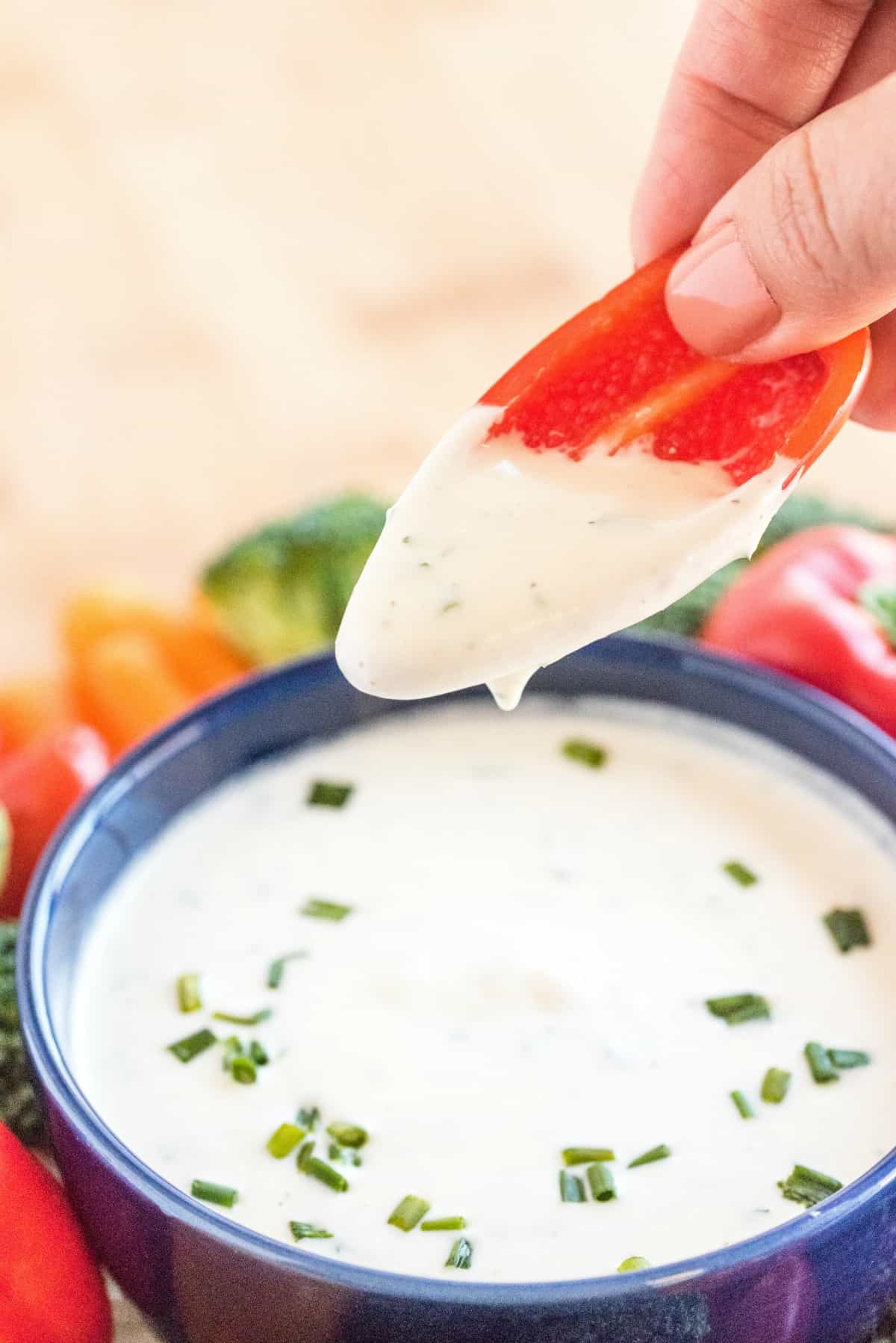 Blue bowl filled with ranch dip and a red pepper being dipped in ranch dressing.