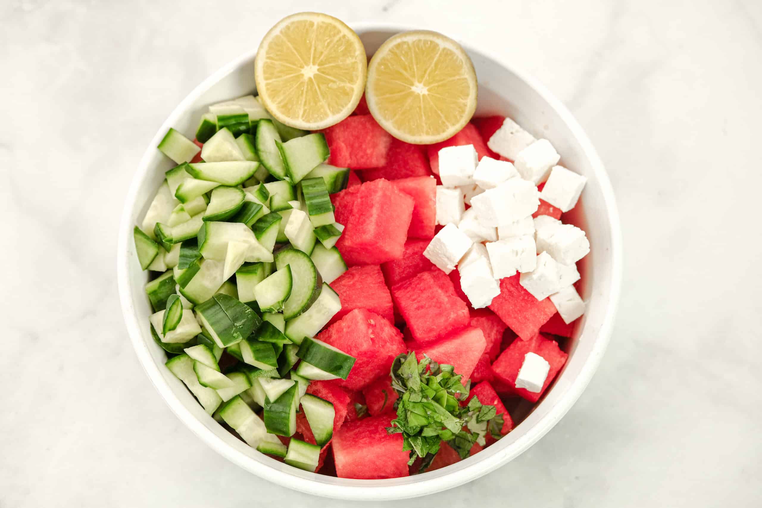 Watermelon salad with ingredients in a white bowl before stirring.