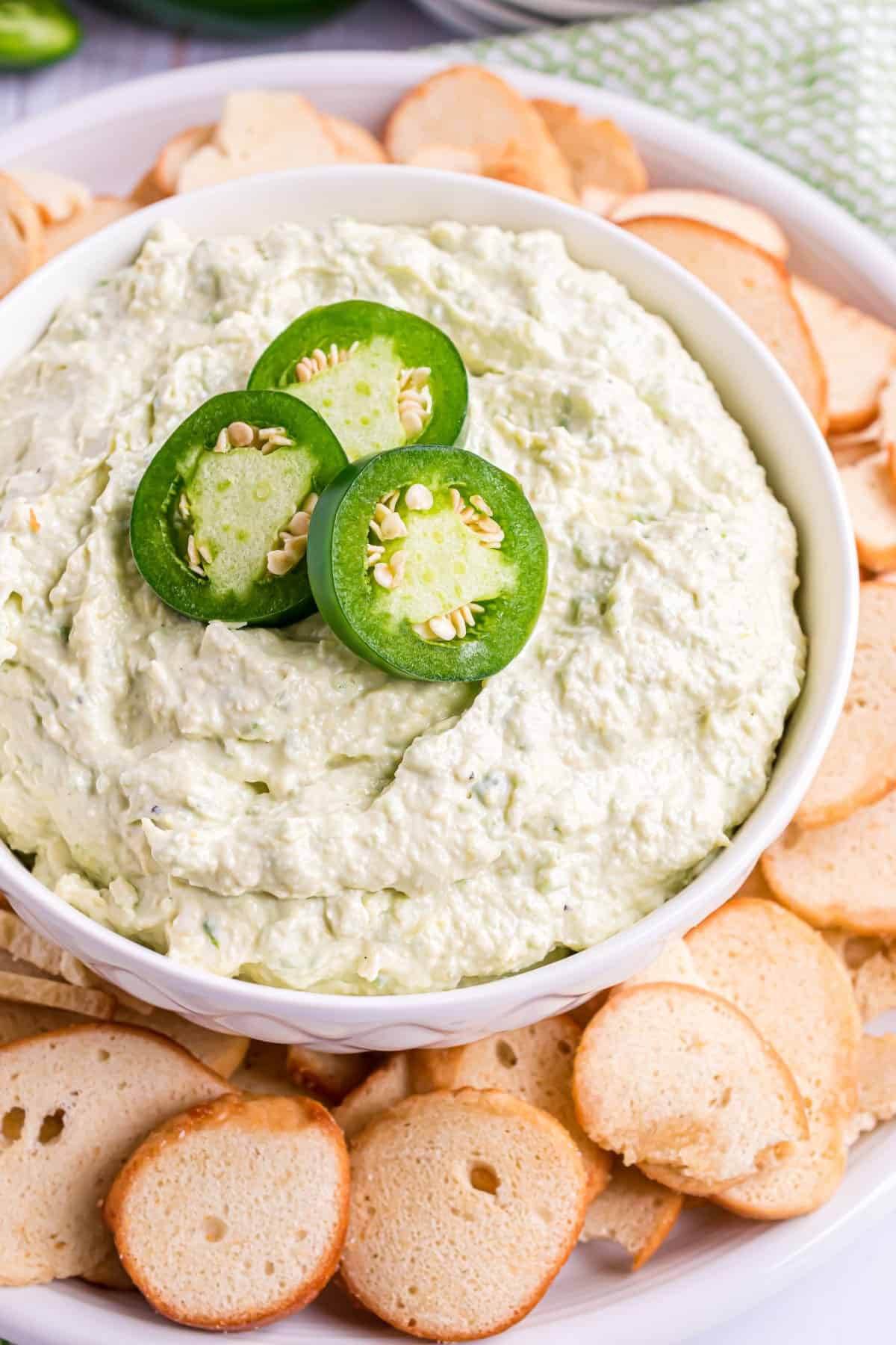 White bowl with artichoke dip and topped with sliced jalapenos. Served with bagel chips.