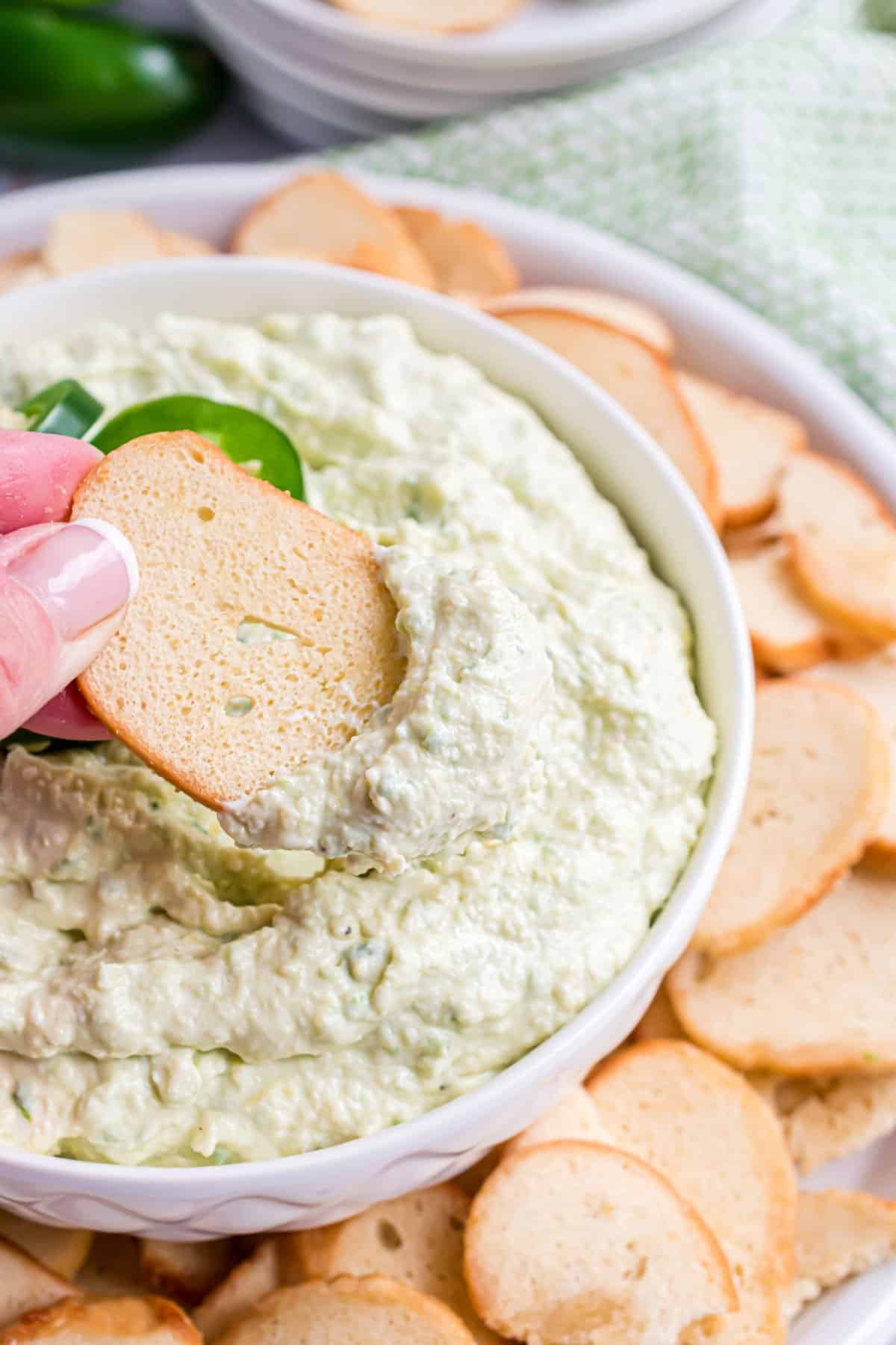 Bagel chip being dipped into jalapeno artichoke dip.