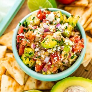 Avocado salsa in a light green bowl with pita chips on the side.
