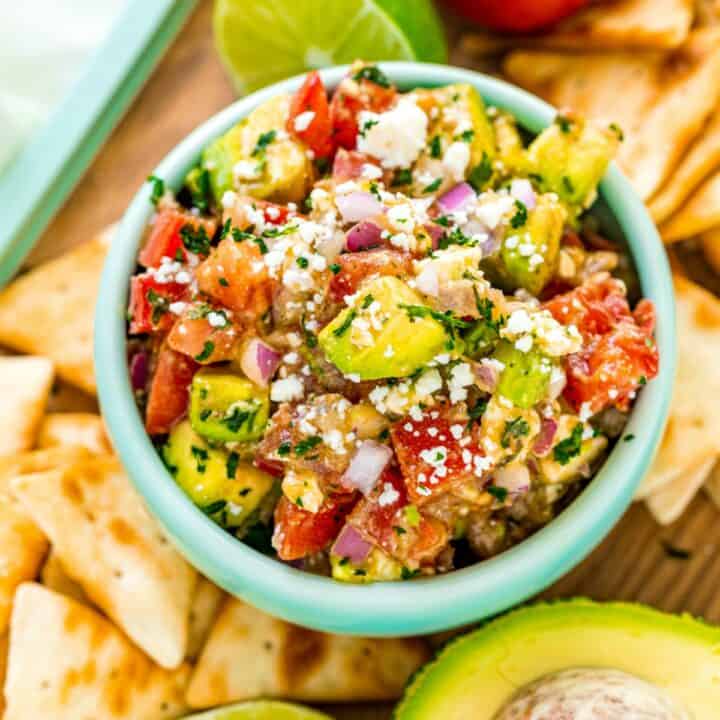 Avocado salsa in a light green bowl with pita chips on the side.