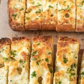 Cheesy garlic bread on parchment paper, sliced.