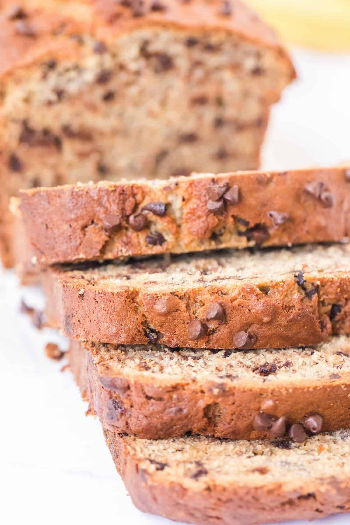 Thick slices of chocolate chip banana bread on a white counter.