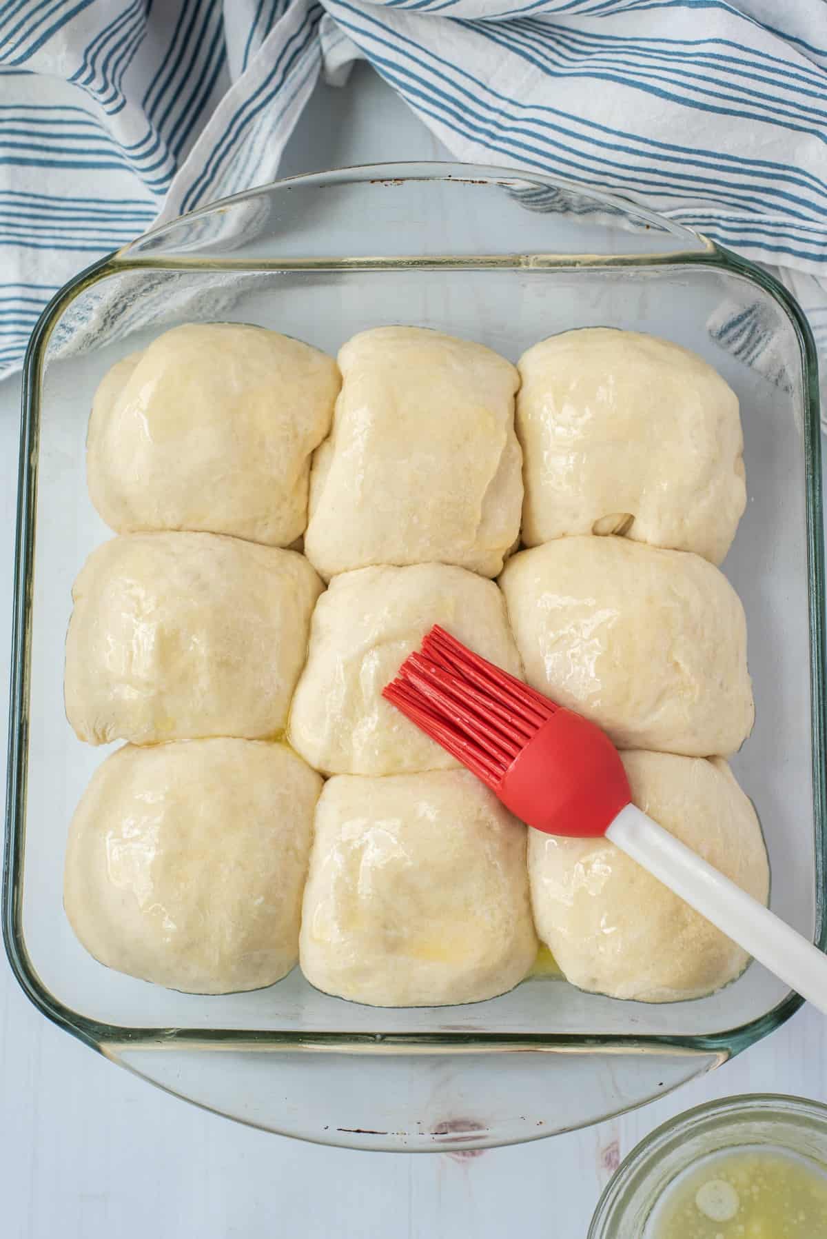 Butter brushed over dinner rolls in a clear glass baking dish.