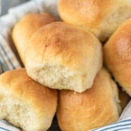 Linen lined basket filled with fluffy dinner rolls.