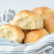 Fluffy light dinner rolls in a linen napkin lined bowl.