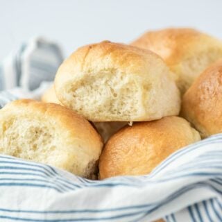 Fluffy light dinner rolls in a linen napkin lined bowl.