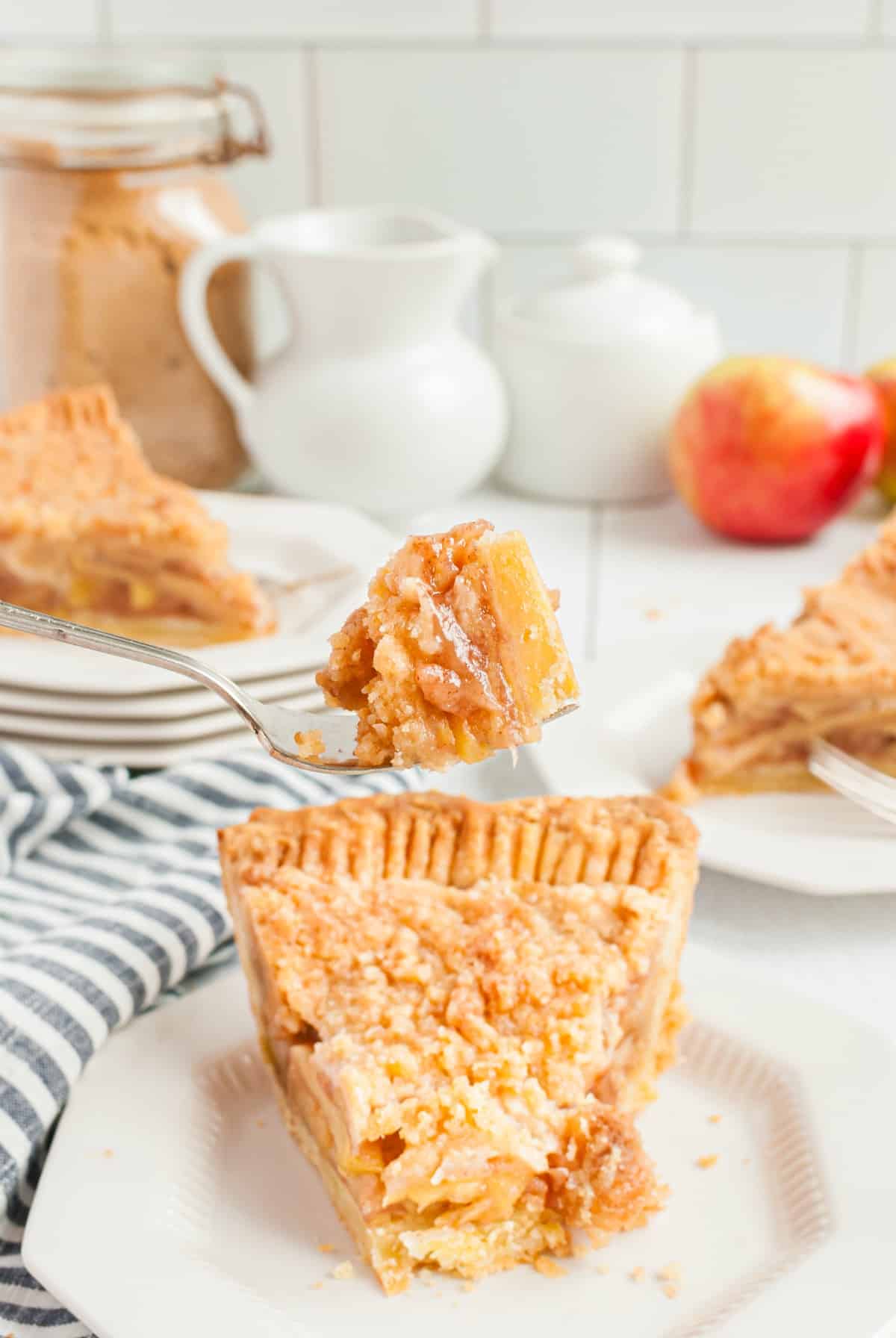 Slice of dutch apple pie on a plate with one forkful of pie being lifted.