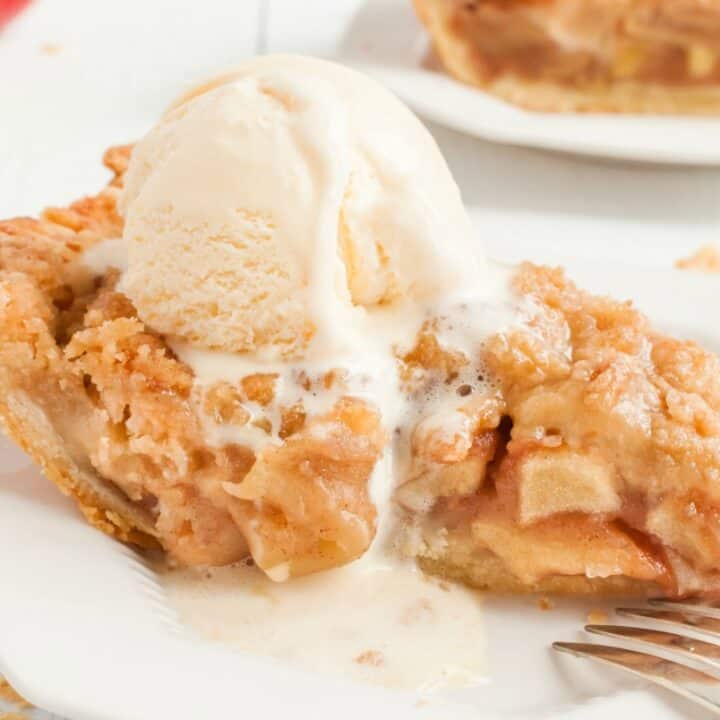 Slice of apple pie on a white dessert plate with a melting scoop of vanilla ice cream on top.