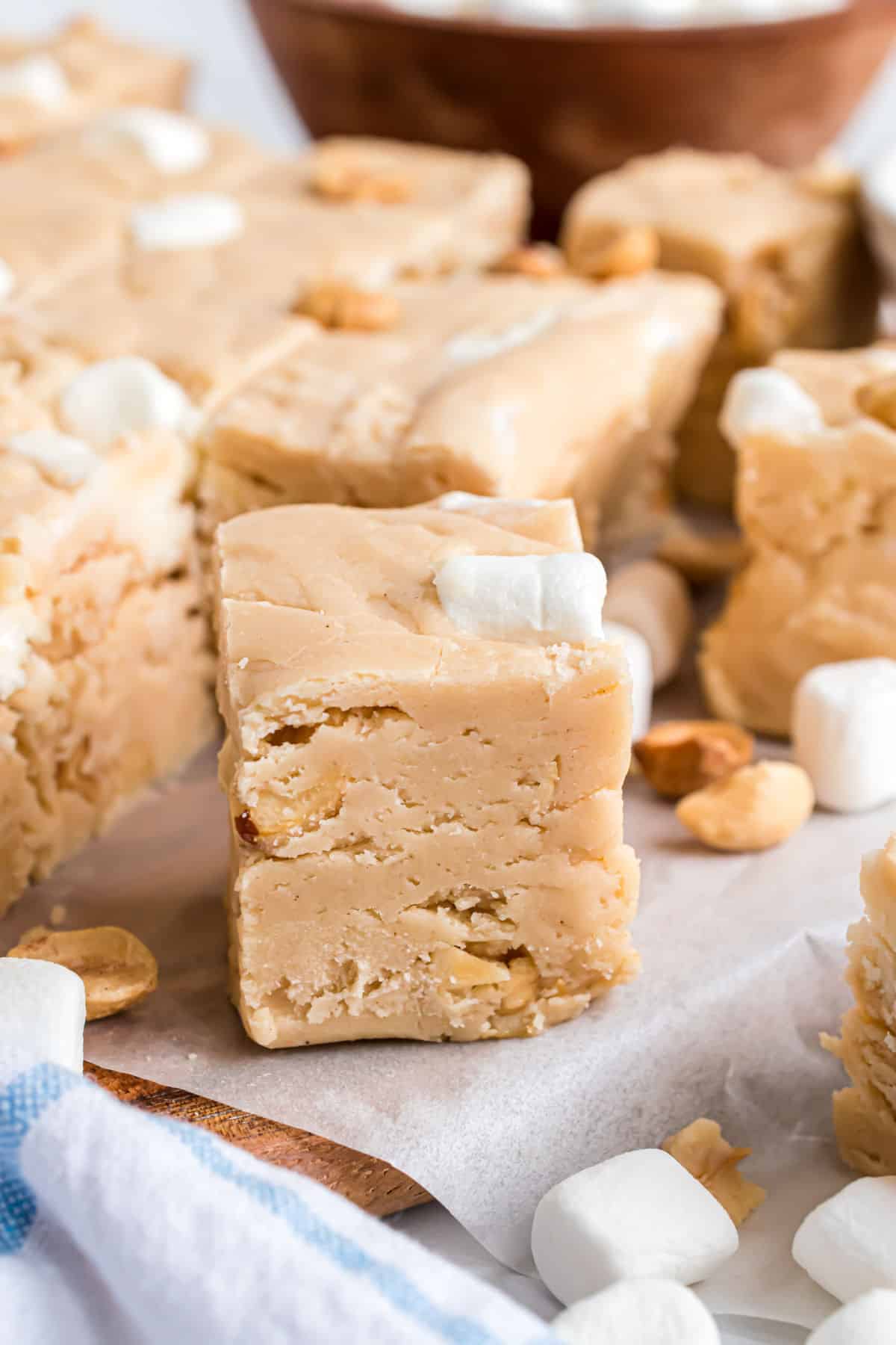 Piece of peanut butter fudge with marshmallow and peanuts on wooden cutting board lined with parchment paper.