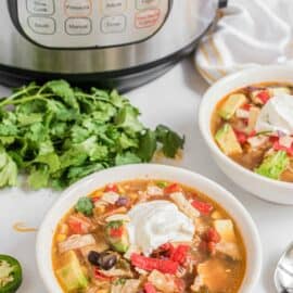 Chicken tortilla soup in a white bowl topped with sour cream, avocado and tortilla strips.