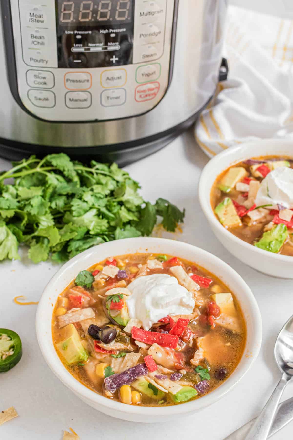 Chicken tortilla soup in a white bowl topped with sour cream, avocado and tortilla strips.