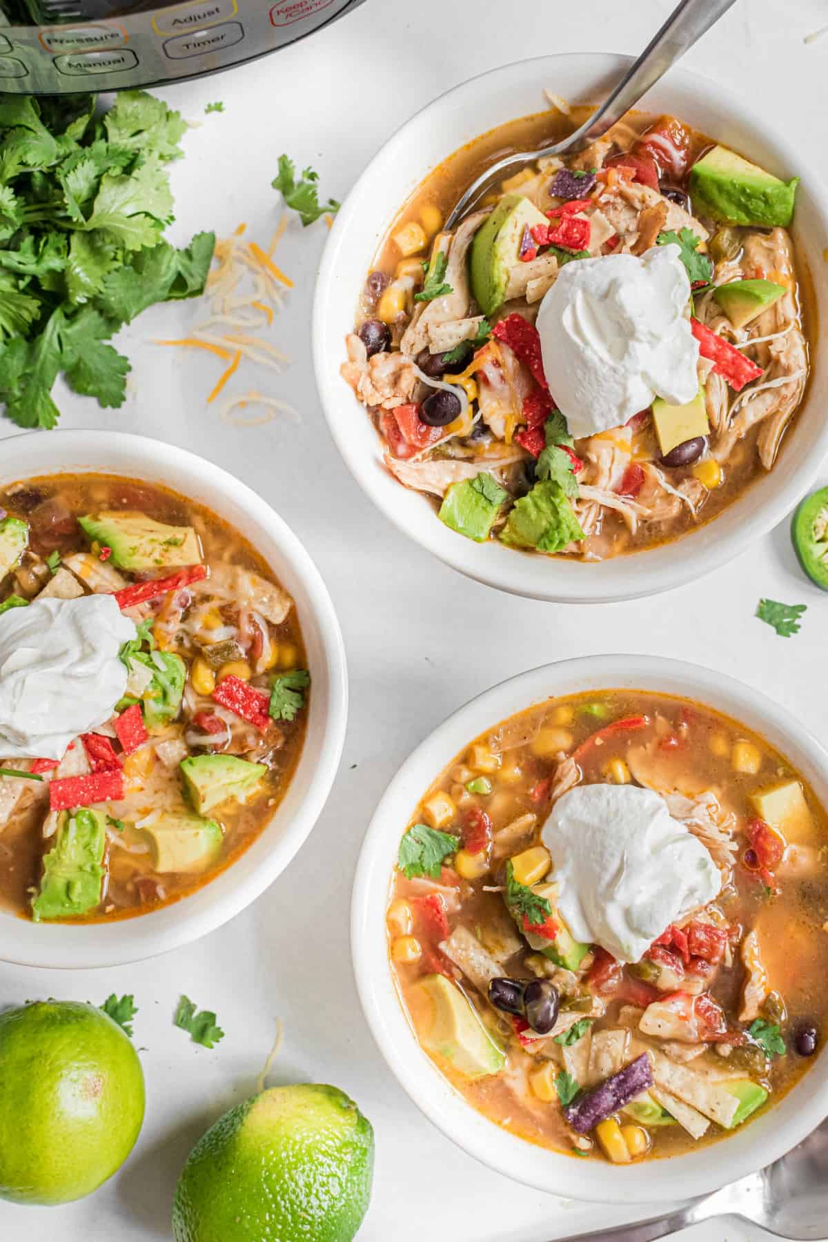 Three white bowls with chicken tortilla soup and toppings.