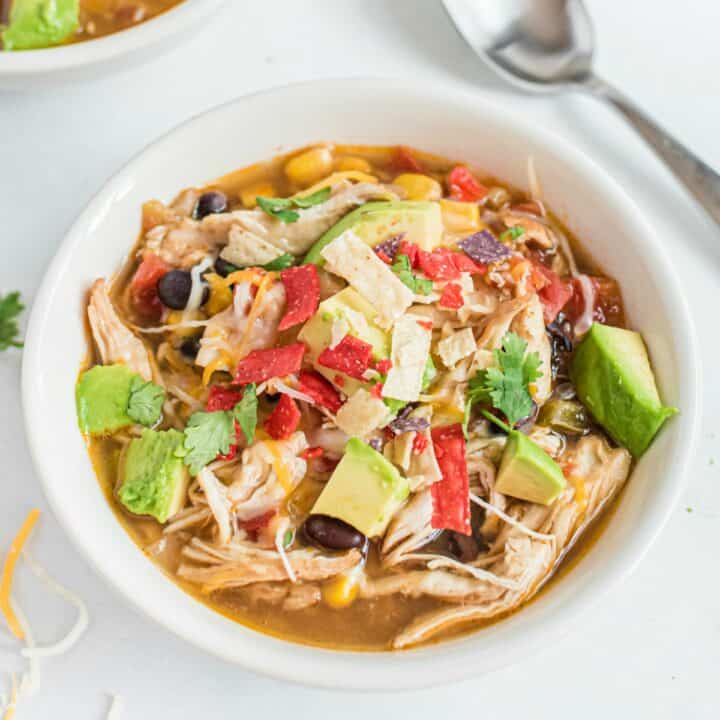 Chicken Tortilla Soup in a white bowl, topped with avocado, sour cream, cheese, and tortilla strips.