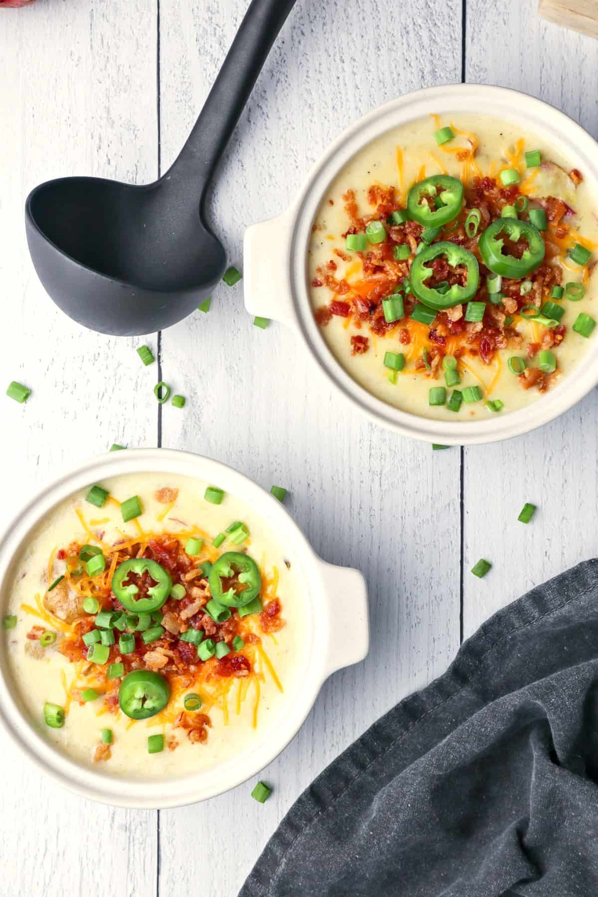 Two individual size crocks of loaded potato soup for serving, with a ladle on the side.