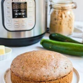 Loaf of zucchini bread on a white plate with instant pot in background.