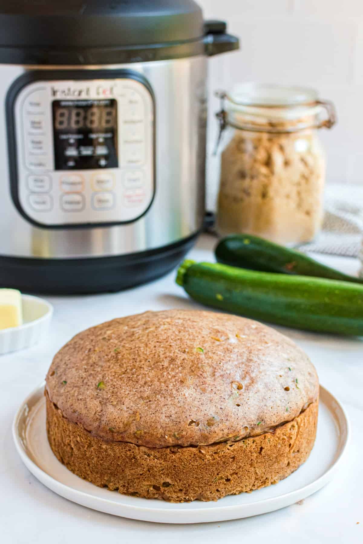 Loaf of zucchini bread on a white plate with instant pot in background.