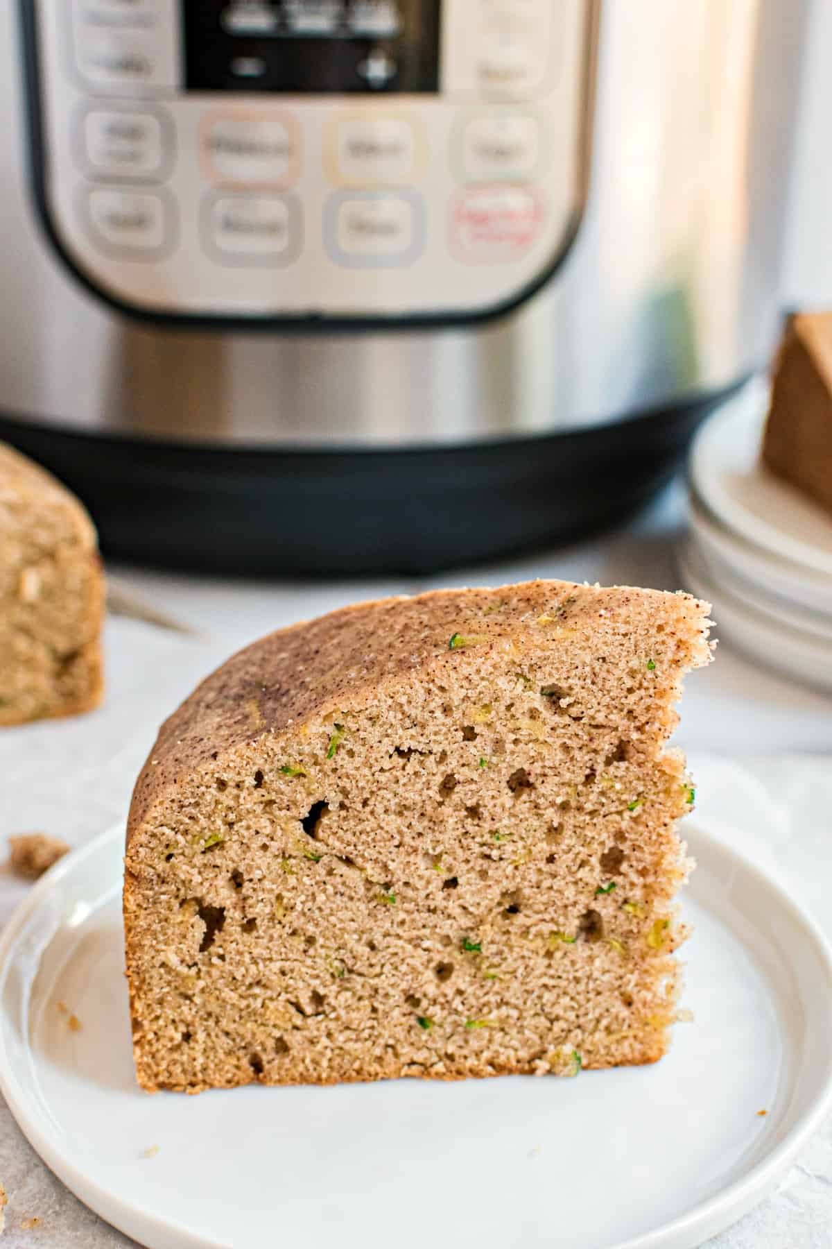 Thick slice of zucchini bread on a white plate with instant pot in background.