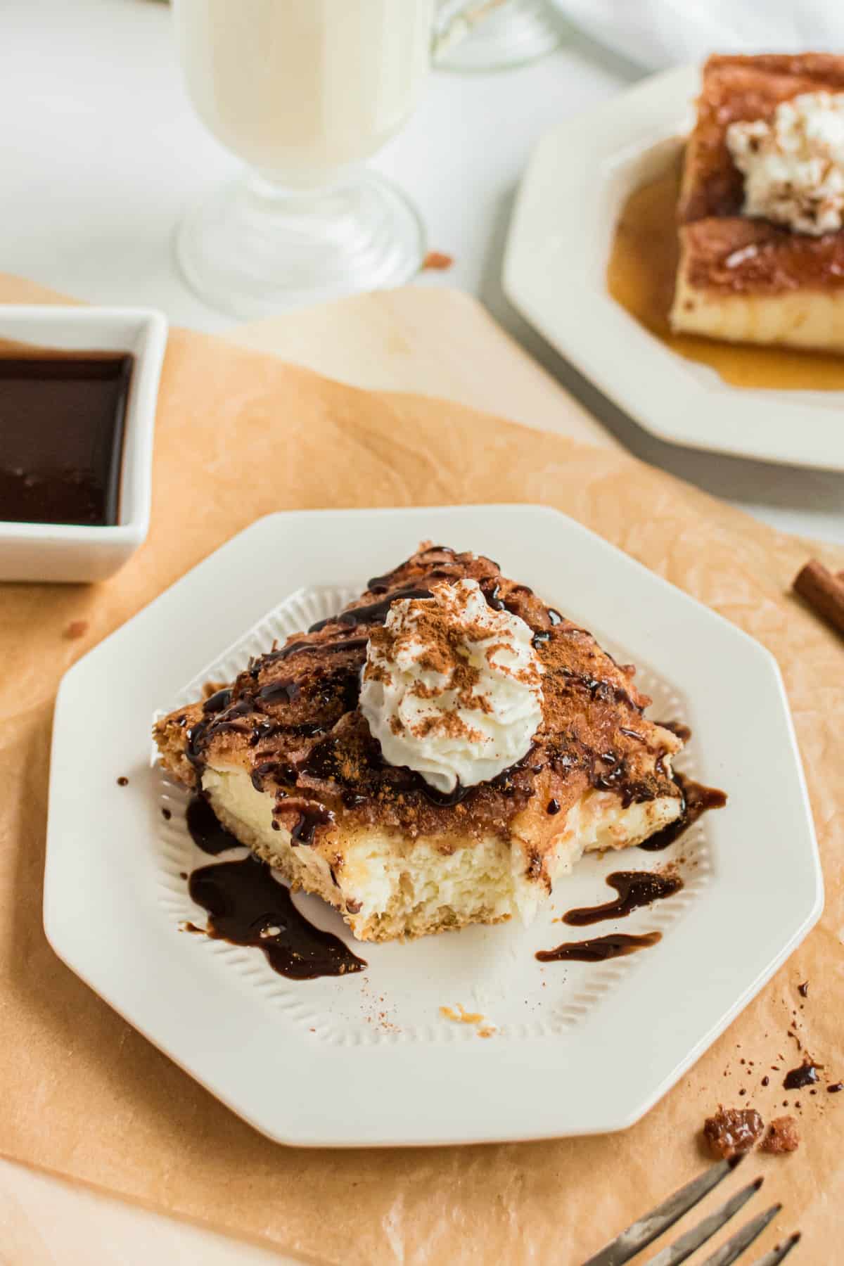 Sopapilla cheesecake bar with one bite removed. Topped with chocolate sauce and whipped cream.