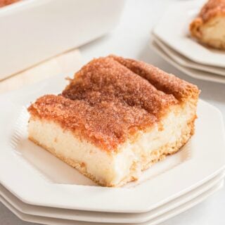 Slice of sopapilla cheesecake on a white plate topped with cinnamon sugar.