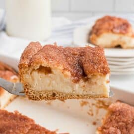 Slice of sopapilla cheesecake being lifted out of a white 13x9 dish with a spatula.