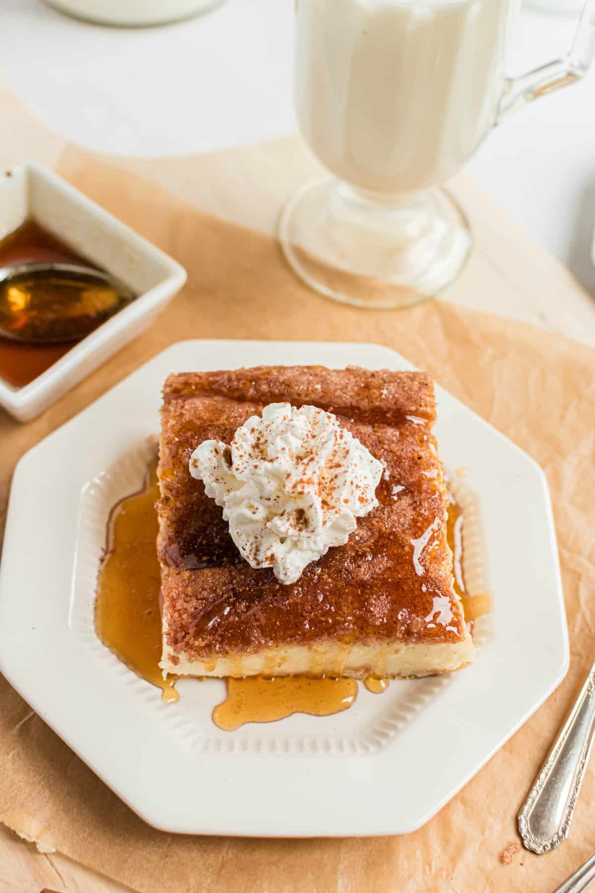 Slice of sopapilla cheesecake bar on a white plate, drizzled with honey and a dollop of whipped cream on top.