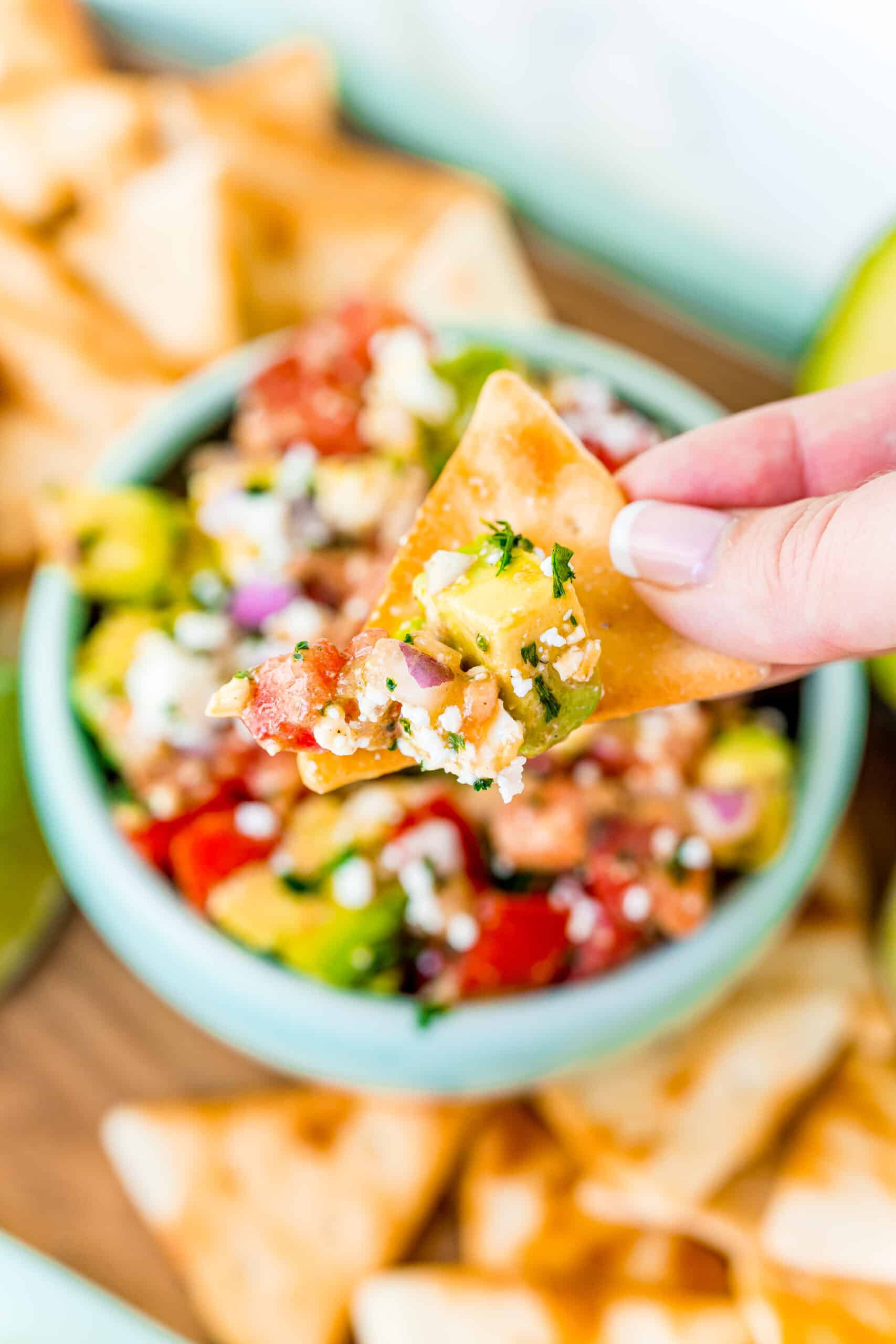 Pita chip being dipped into avocado salsa.