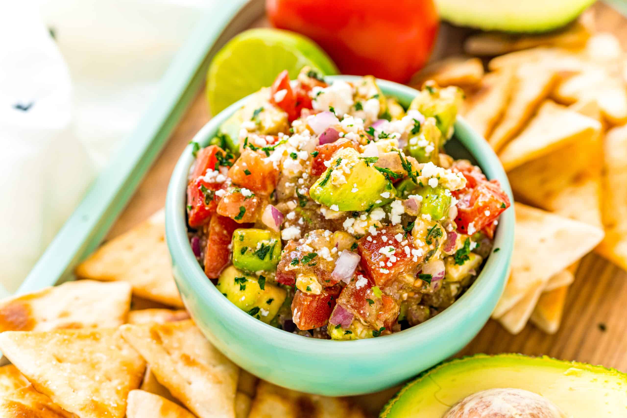 Chunky guacamole salsa in a light teal bowl with pita chips on the side.