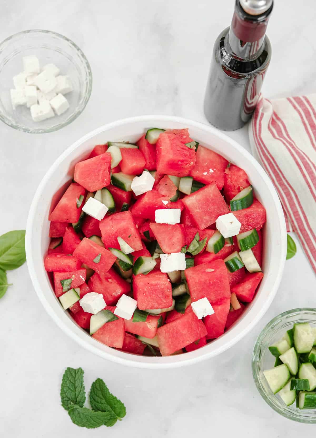 Watermelon salad with feta, cucumber, mint, basil, and lime juice in a white bowl.