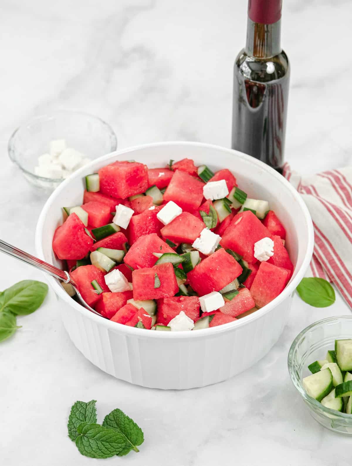 Watermelon salad in a white bowl with feta, cucumber, lime juice and herbs.