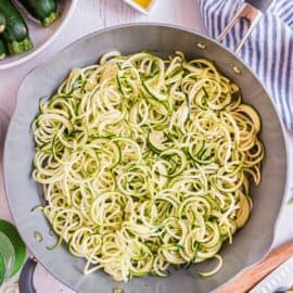Zucchini noodles in a skillet with olive oil on side.