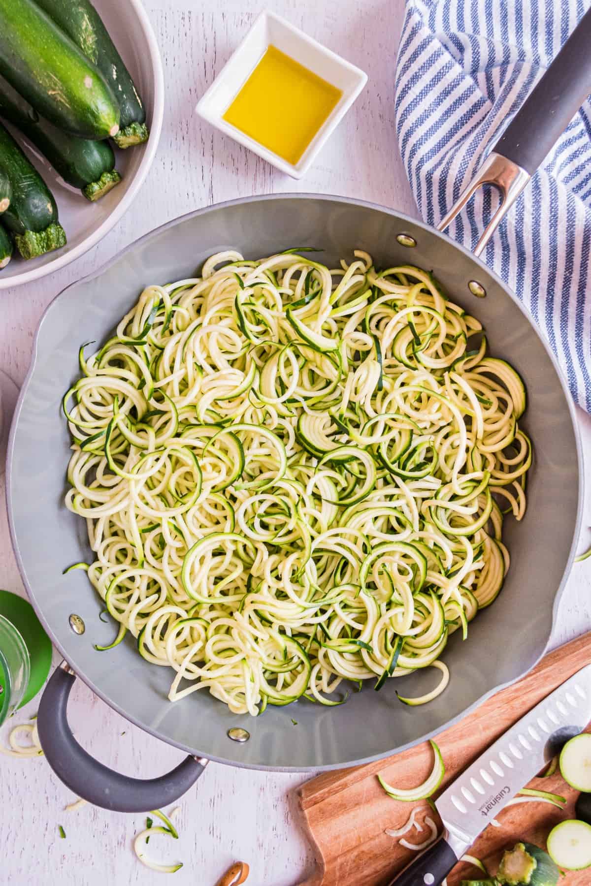 Zucchini noodles in a skillet with olive oil on side.