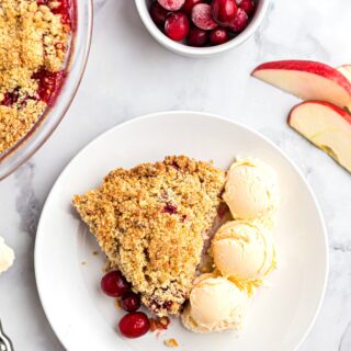 Three scoops of vanilla ice cream on a plate with a slice of apple cranberry crumble.