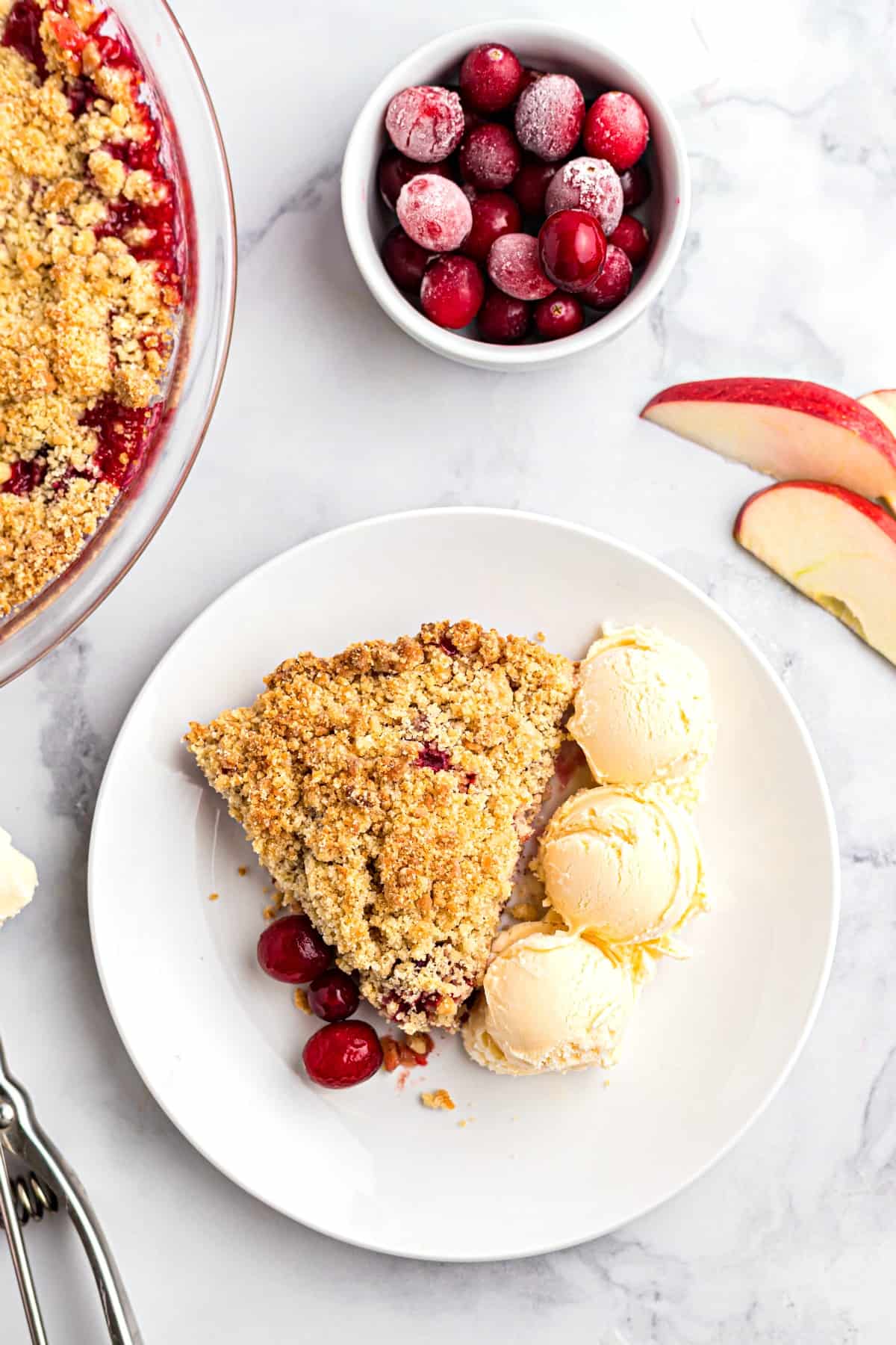 Three scoops of vanilla ice cream on a plate with a slice of apple cranberry crumble.