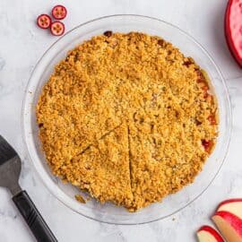 Apple cranberry crumble baked in a glass pie plate and served on a marble counter.