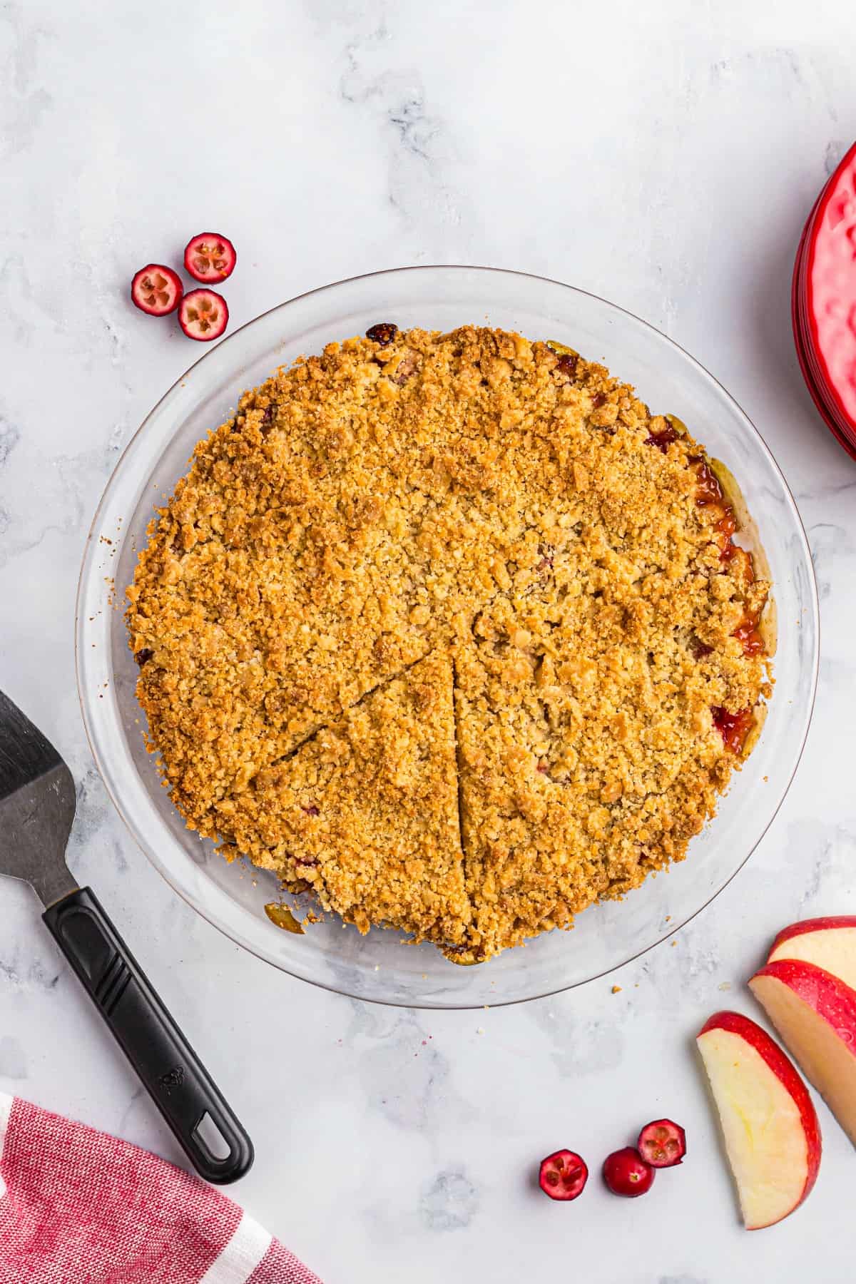 Apple cranberry crumble baked in a glass pie plate and served on a marble counter.