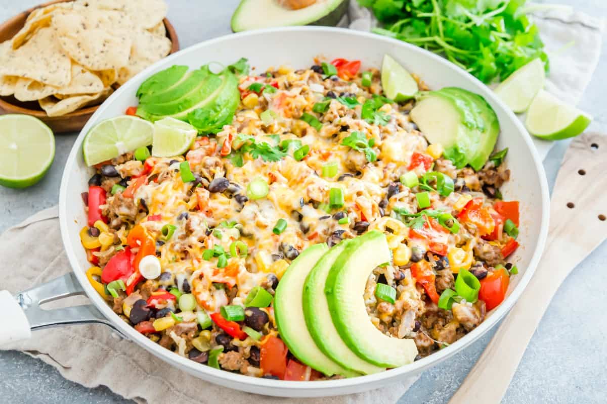 Beef Taco skillet in a white skillet topped with avocado and served with tortilla chips.