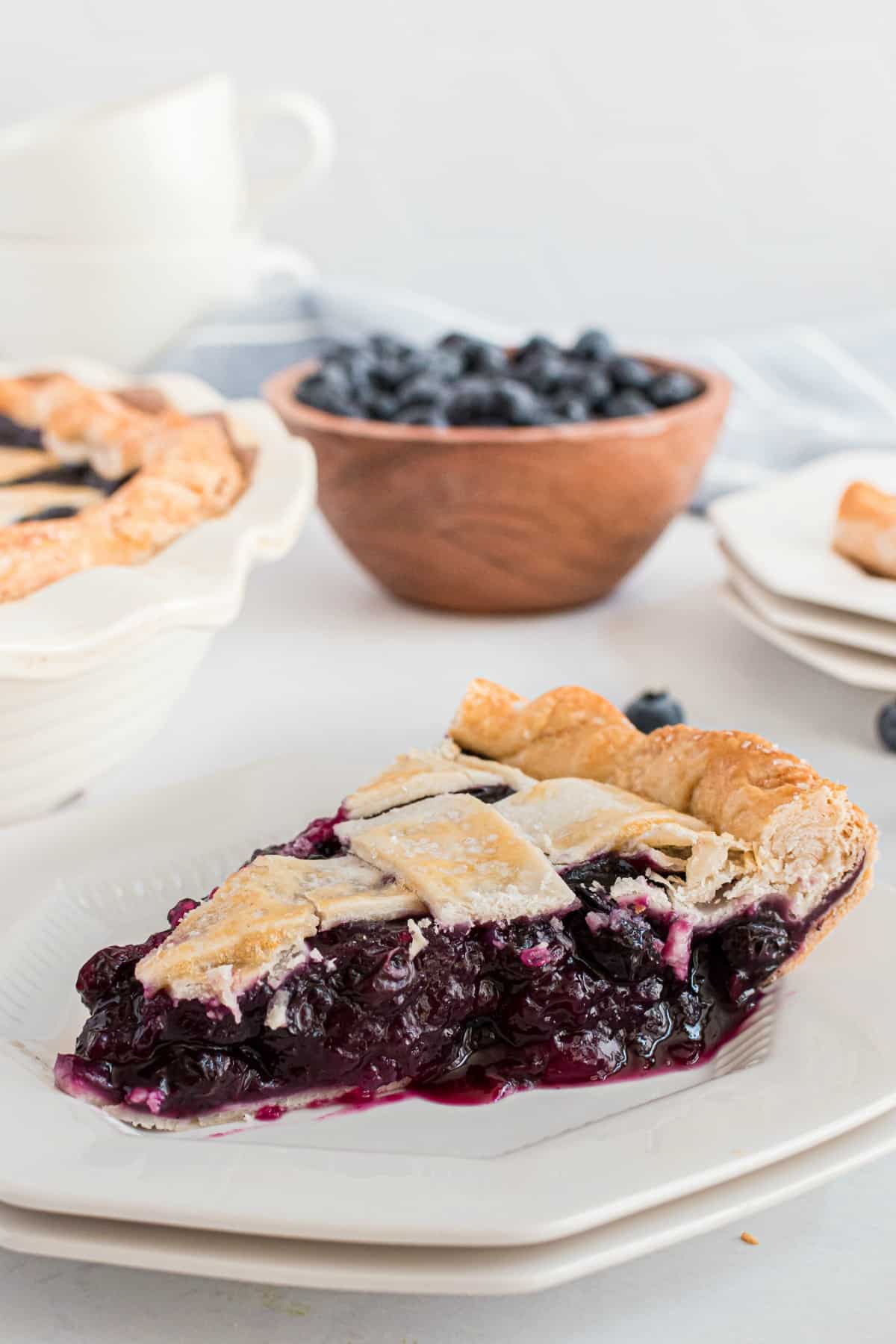 Slice of deep dish blueberry pie with lattice topped crust on a white plate.