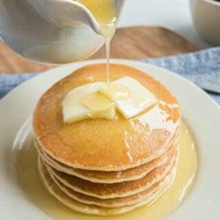 Stack of buttermilk pancakes being topped with a pour of buttermilk syrup.