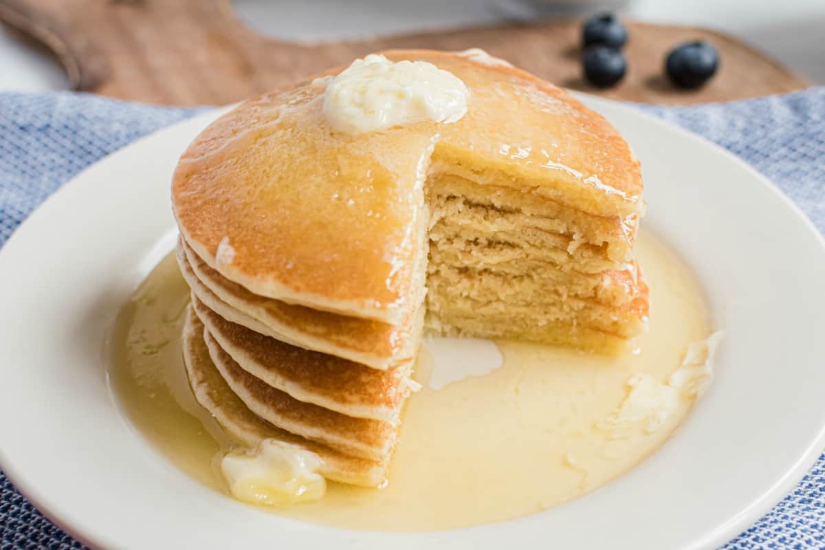 Stack of pancakes with a bite removed and covered in buttermilk syrup.