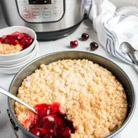 Cherry cobbler in a springform pan with one scoop missing and instant pot in background.